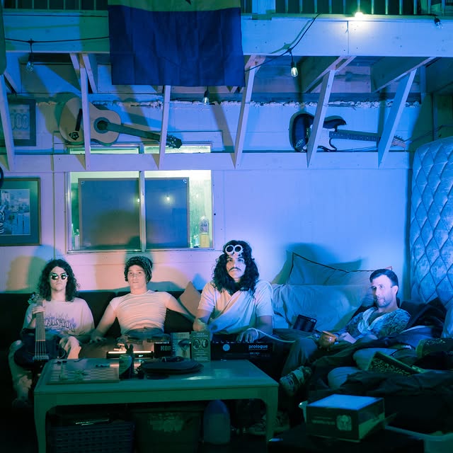 SHWING — four of the band lounging with guitars and a synth in a blue-lit garage